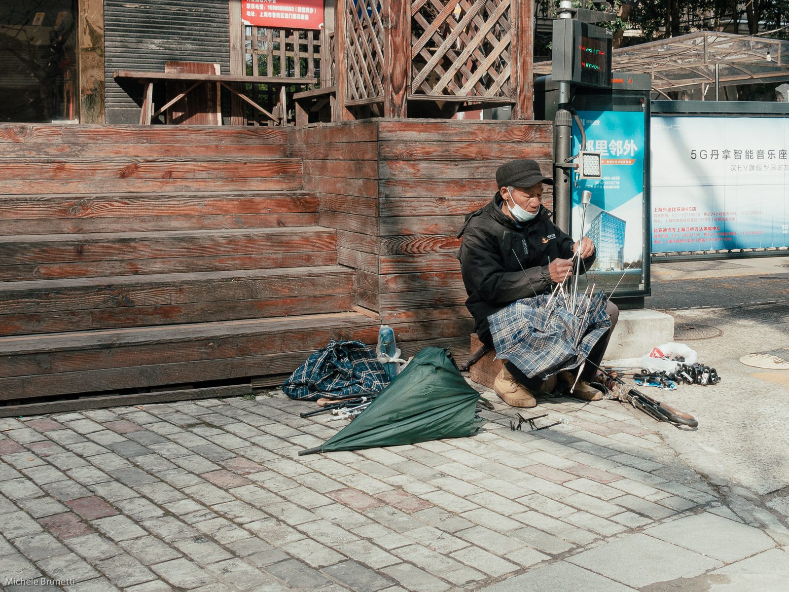 Michele Brunetti - An elderly man, hoping to make some money, repairs old umbrellas in Shanghai, where umbrellas are practically given away everywhere.